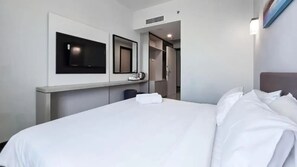 Une chambre d’hôtel comprenant un lit, un téléviseur à écran plat fixé au mur, un miroir et une armoire.