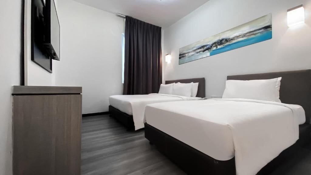 A hotel room with two beds, a desk, a painting on the wall, and a window with curtains.