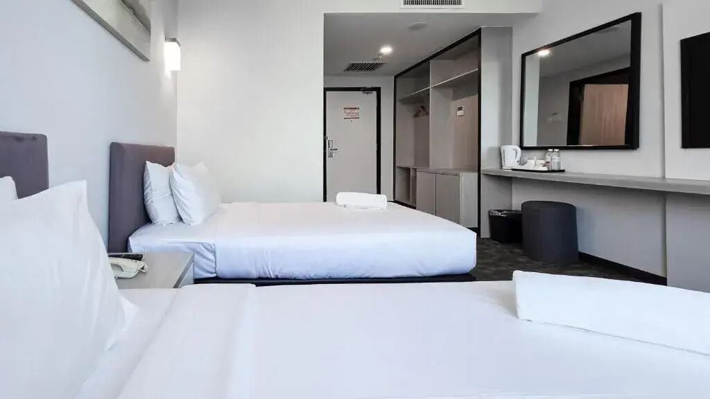 Ein Hotelzimmer mit einem Bett, einem Nachttisch mit Telefon, einem Spiegel, einem Kleiderschrank und einem Papierkorb.