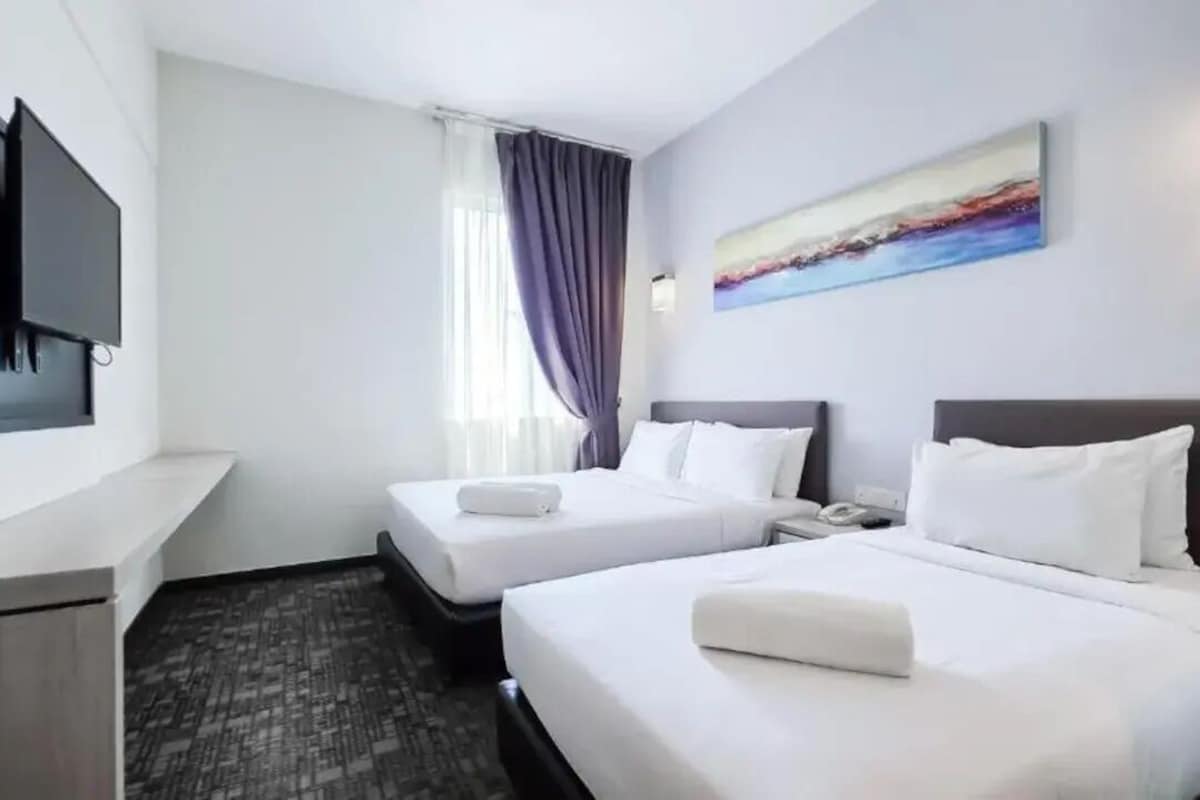 A hotel room with two beds, a flat-screen TV mounted on the wall, a painting above the beds, and a window with curtains.