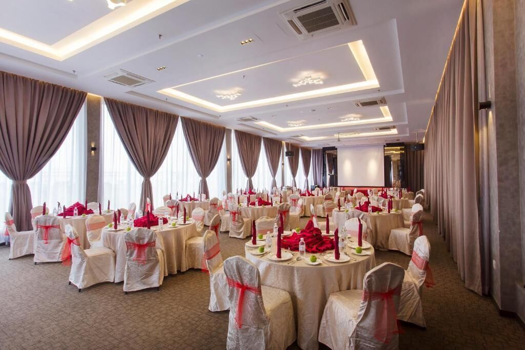Un salón de banquetes con mesas redondas, sillas y un escenario.
