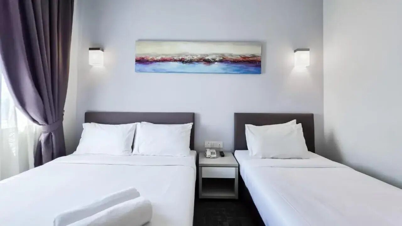 Ein Hotelzimmer mit zwei Betten, einem Nachttisch, einem Bild an der Wand und einem Fenster mit Vorhängen.