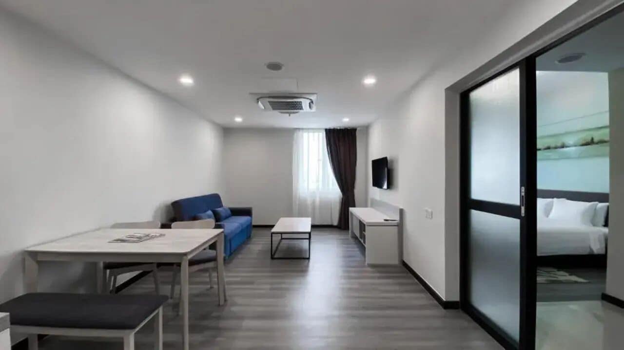 Habitación de hotel con cama, escritorio, silla, sofá, televisor y puerta corrediza que da a un balcón.