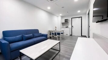 A modern living room with a blue sofa, a white coffee table, and a dining area with a white table and chairs.