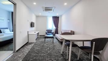 Quarto de hotel com cama, escrivaninha, cadeira, sofá e janela com cortinas.