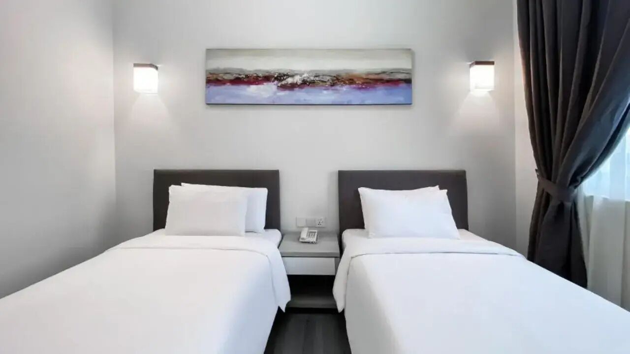 A hotel room with two beds, a painting on the wall, and a phone on the nightstand.