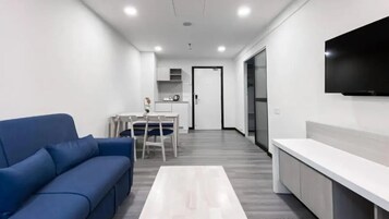 Una sala de estar moderna con un sofá azul, una mesa de centro blanca y una zona de cocina con una mesa de comedor y sillas.