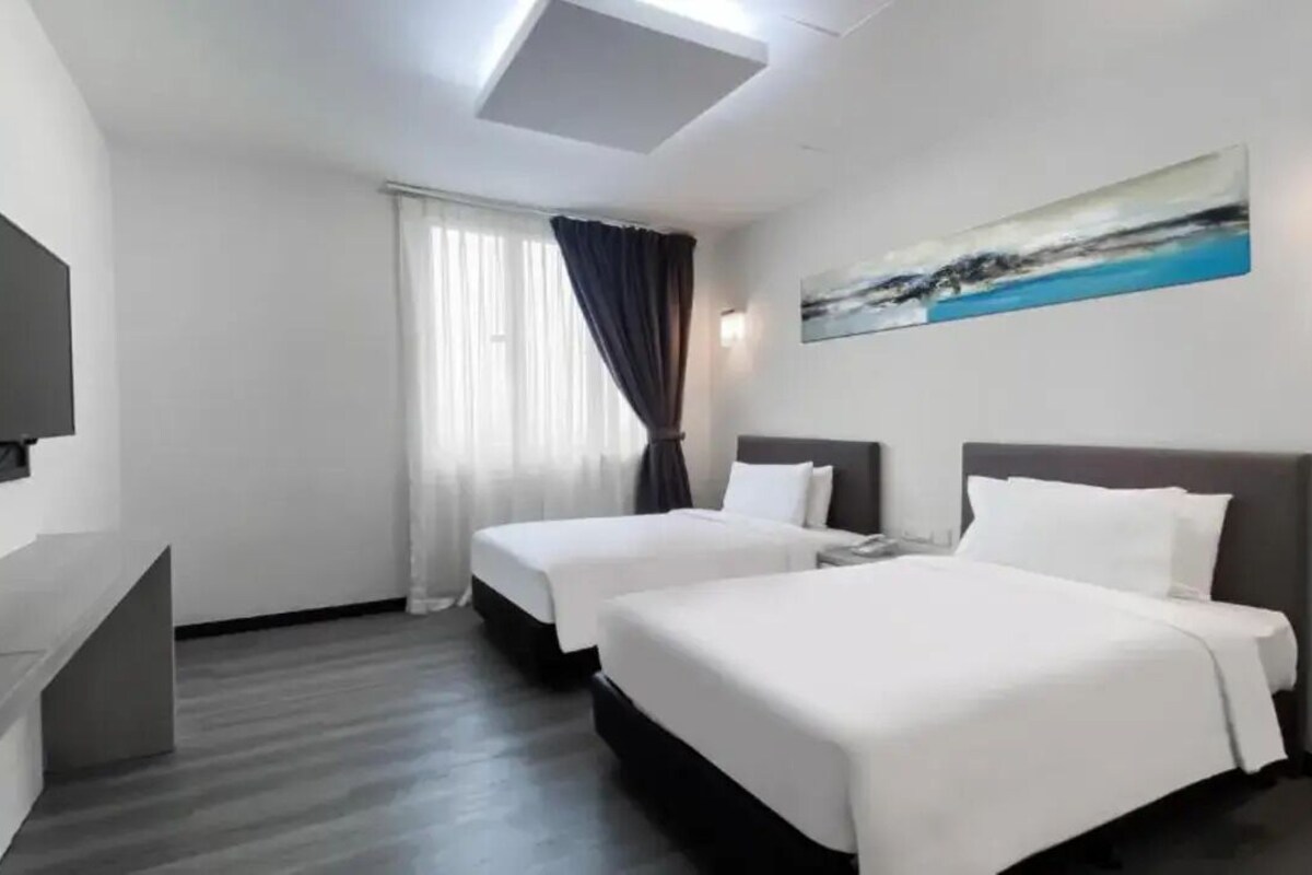 A hotel room with two beds, a flat-screen TV, a painting on the wall, and a window with curtains.