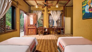 A room with two beds, a desk, chairs, a ceiling fan, and windows with curtains.