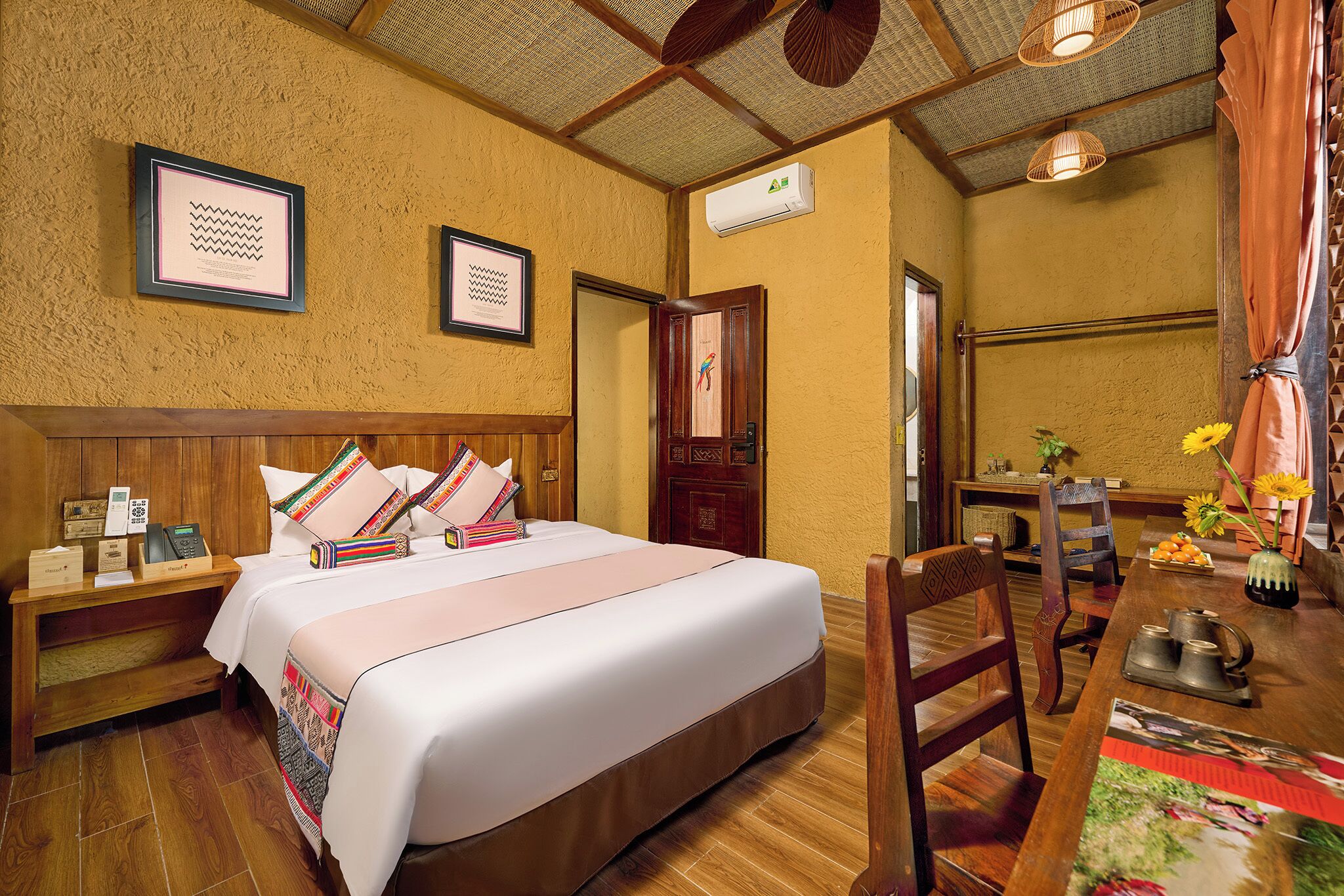 Een hotelkamer met een houten bed, een bureau met een bloevas en een wandairconditioner.
