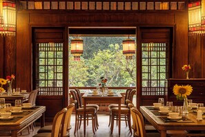 Un comedor tradicional con muebles de madera, una mesa dispuesta para dos personas y vistas a un jardín exuberante a través de amplias ventanas.