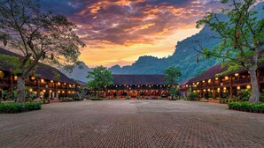 A traditional building with a courtyard, surrounded by trees and a mountainous backdrop.