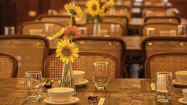 A dining area with tables set for service, featuring floral centerpieces and a warm, dimly lit ambiance.