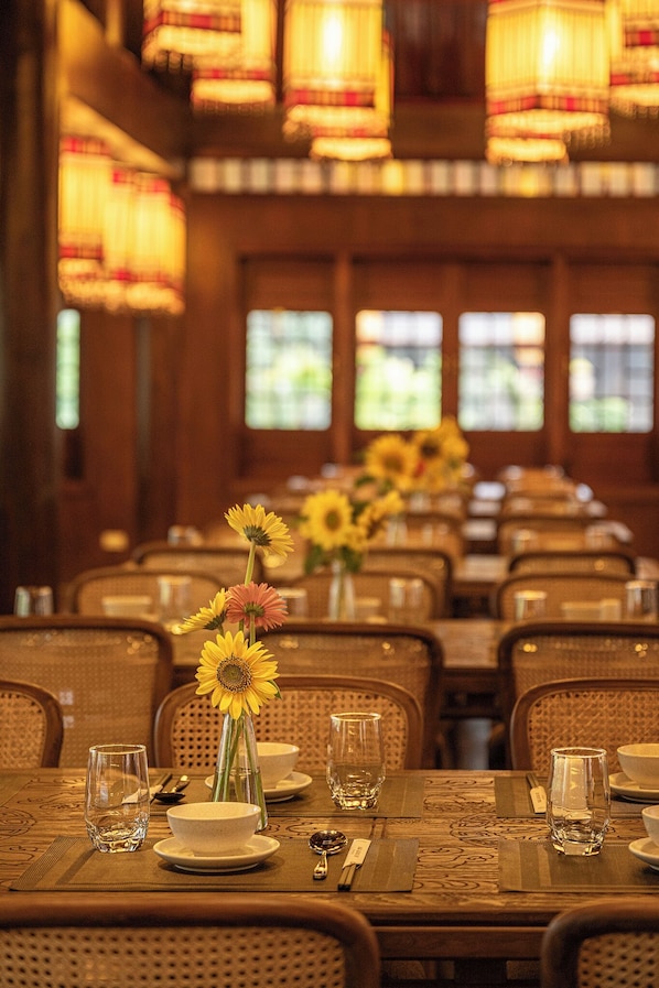 A dining area with tables set for service, featuring floral centerpieces and a warm, dimly lit ambiance.