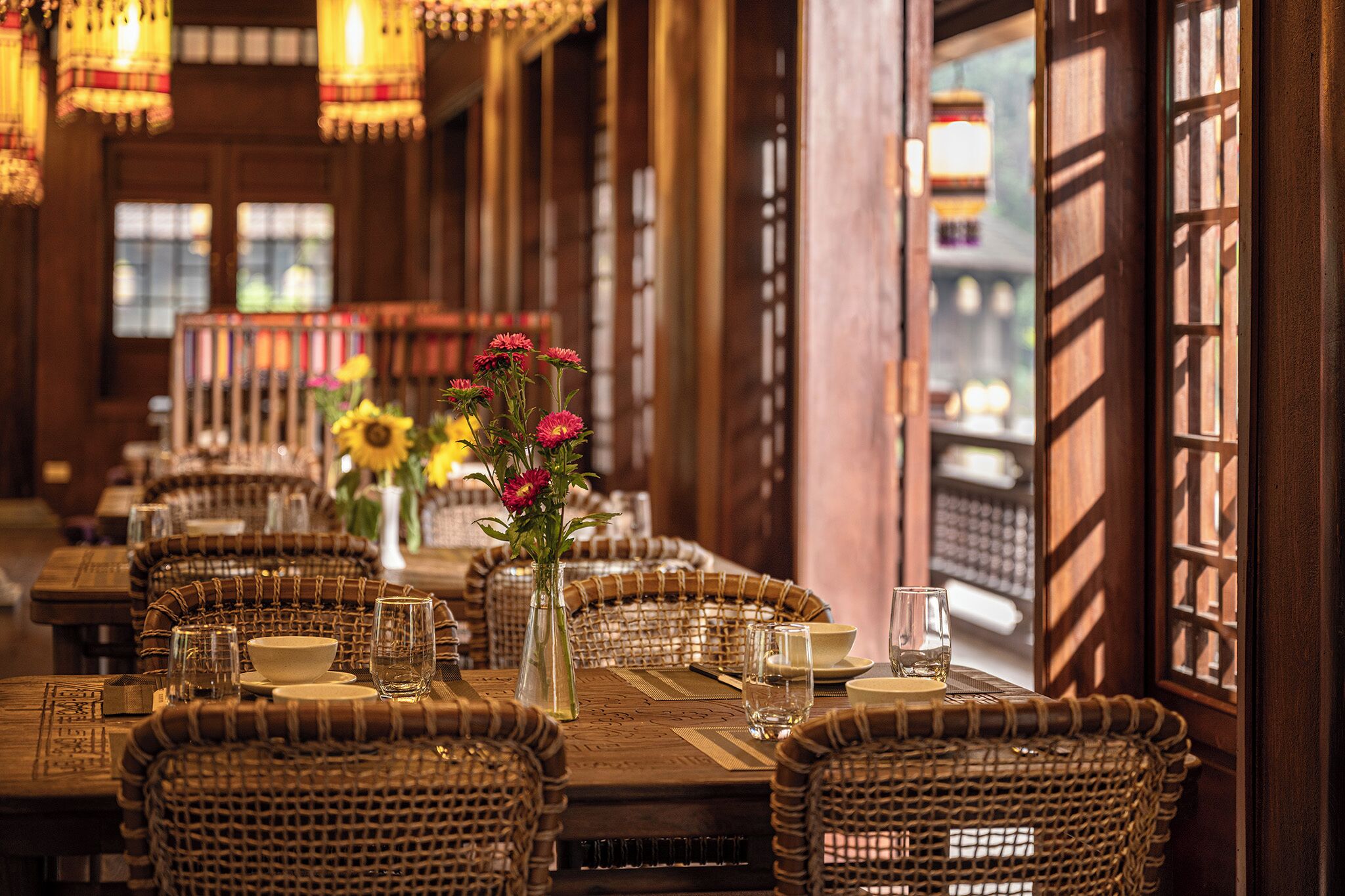 A restaurant with long wooden tables, wicker chairs, and a warm ambiance.