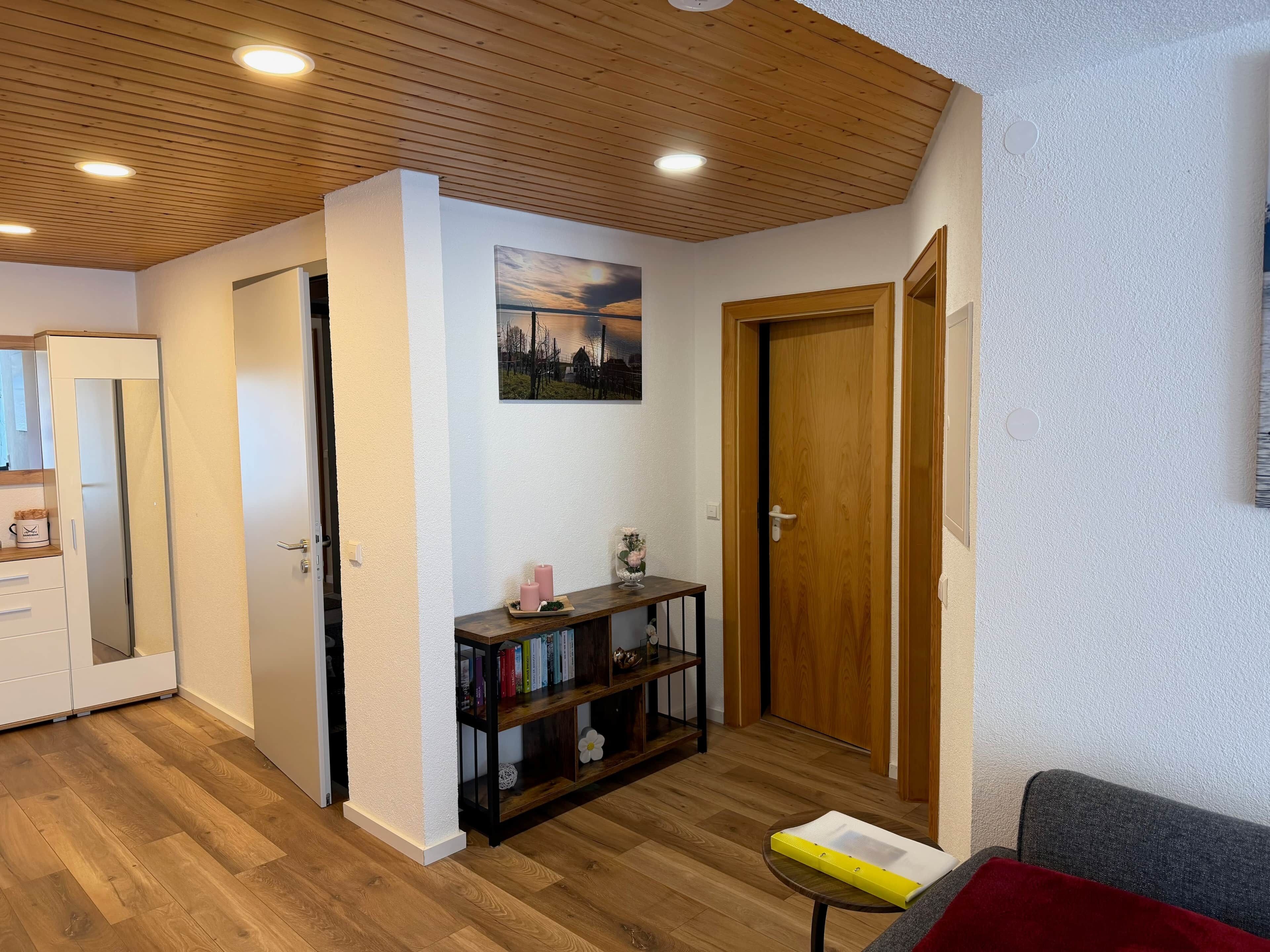 Quarto com teto de madeira, uma estante, uma porta e uma pequena mesa.