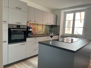 Eine moderne Küche mit Einbauofen, einer Kaffeemaschine und einem Weinglas auf der Arbeitsplatte.