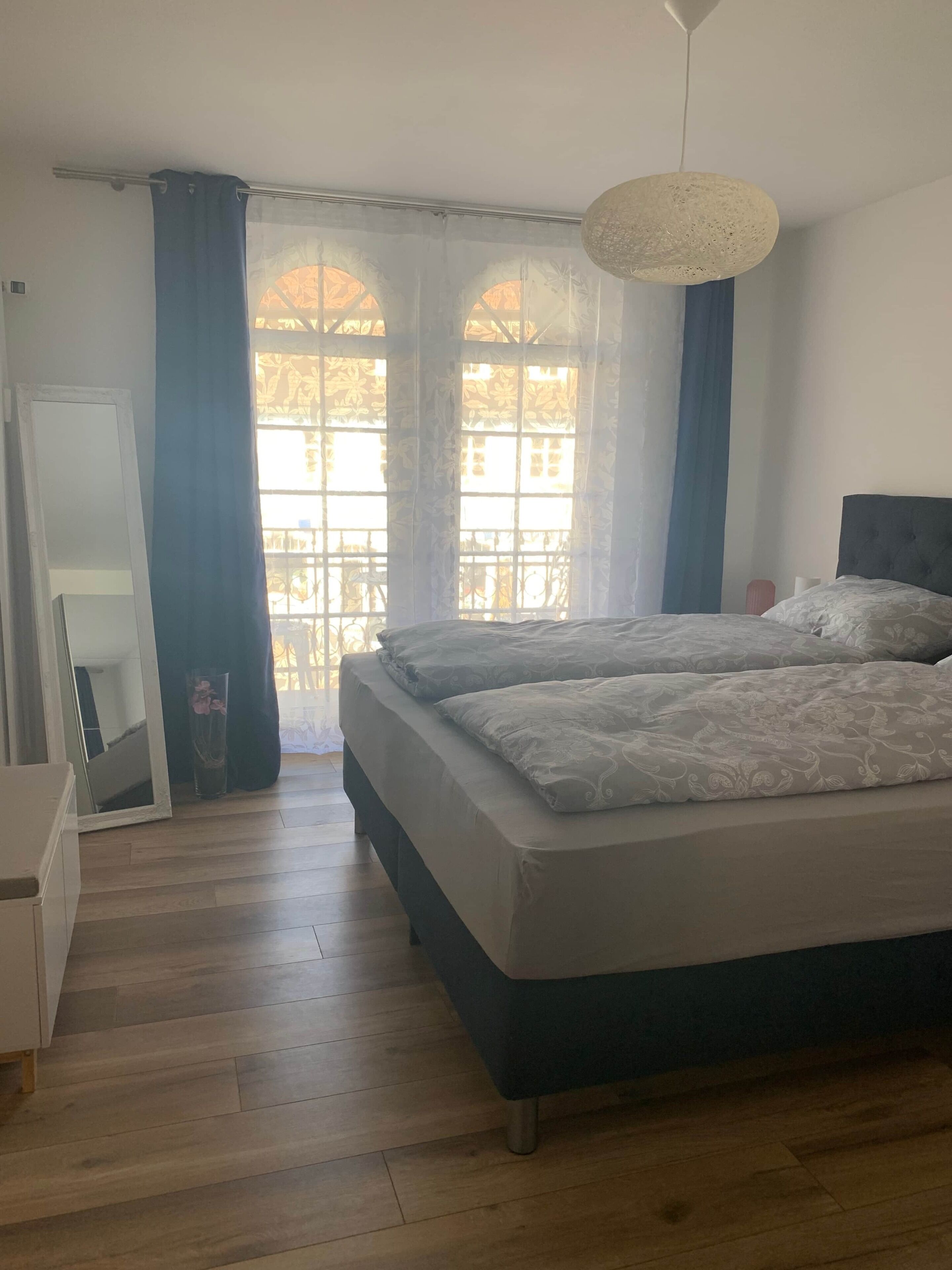 Ein Schlafzimmer mit einem Bett, einem Schminktisch, einem Spiegel und einem Fenster mit Vorhängen.