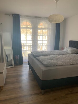 Ein Schlafzimmer mit einem Bett, einem Schminktisch, einem Spiegel und einem Fenster mit Vorhängen.