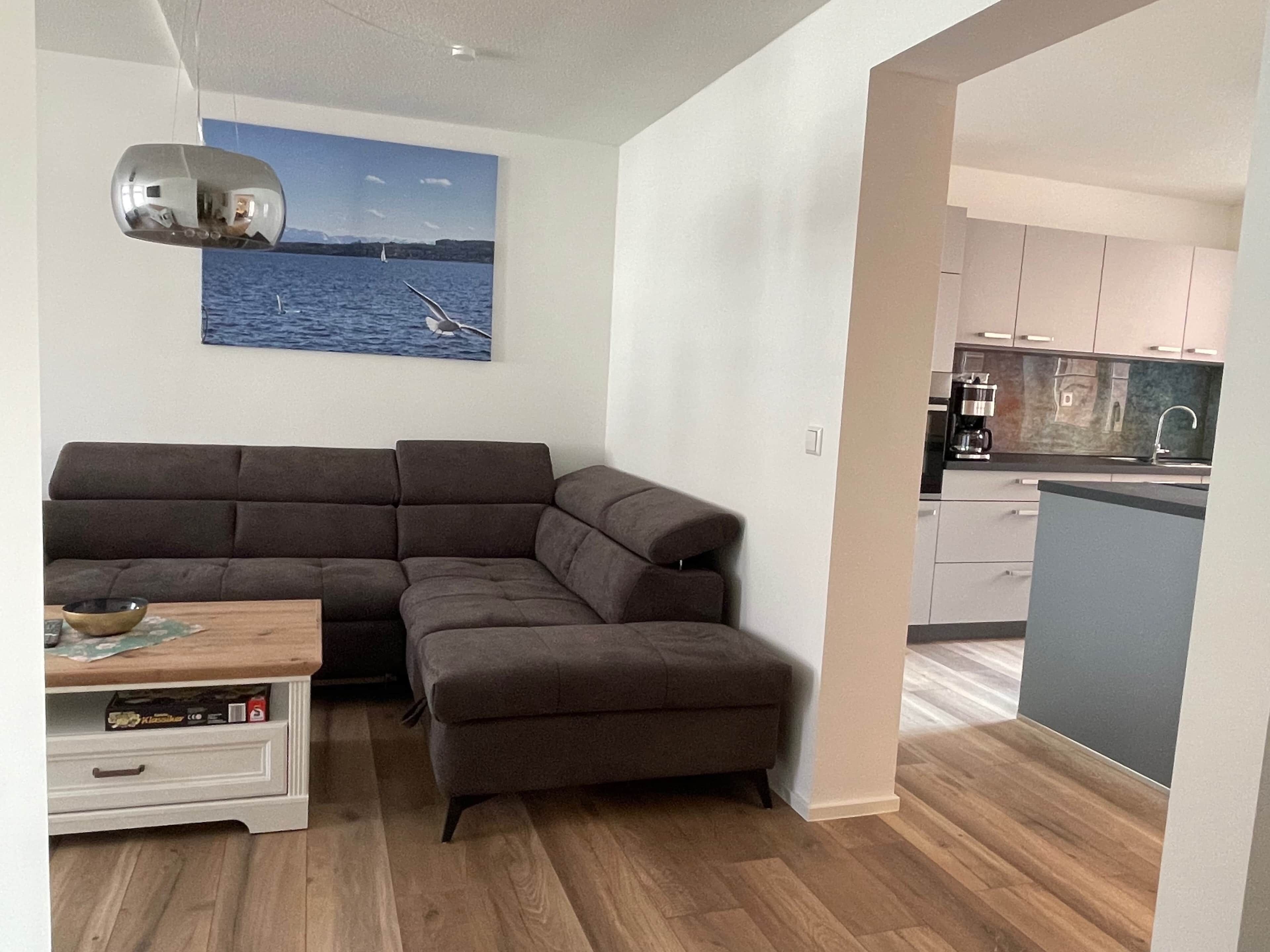 Ein modernes Wohnzimmer mit einem Ecksofa, einem kleinen Tisch und einem Seestück.