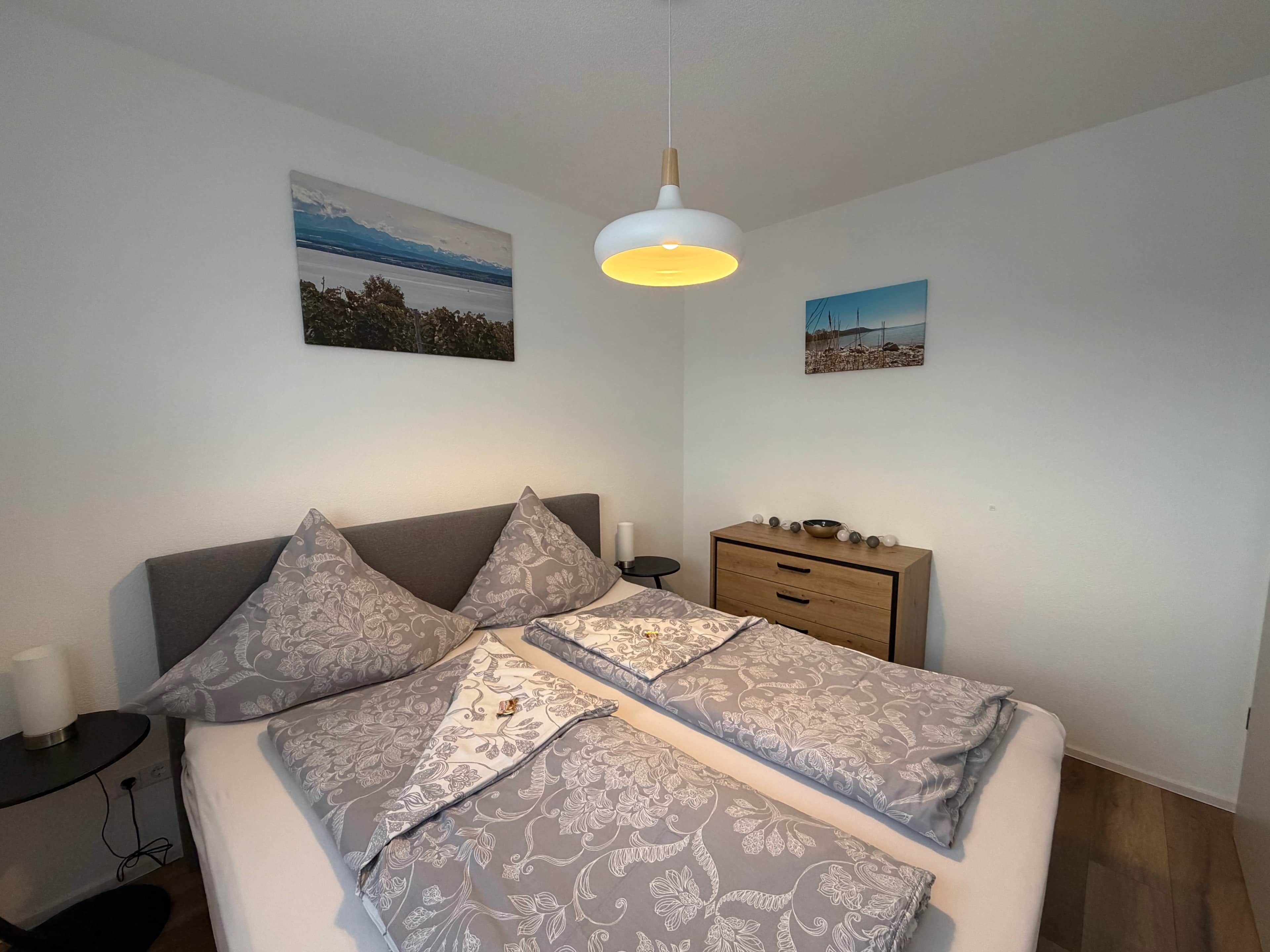 A neatly arranged bedroom with a bed, bedside tables, a dresser, and wall art.