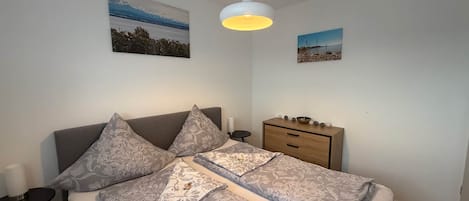 A neatly arranged bedroom with a bed, bedside tables, a dresser, and wall art.