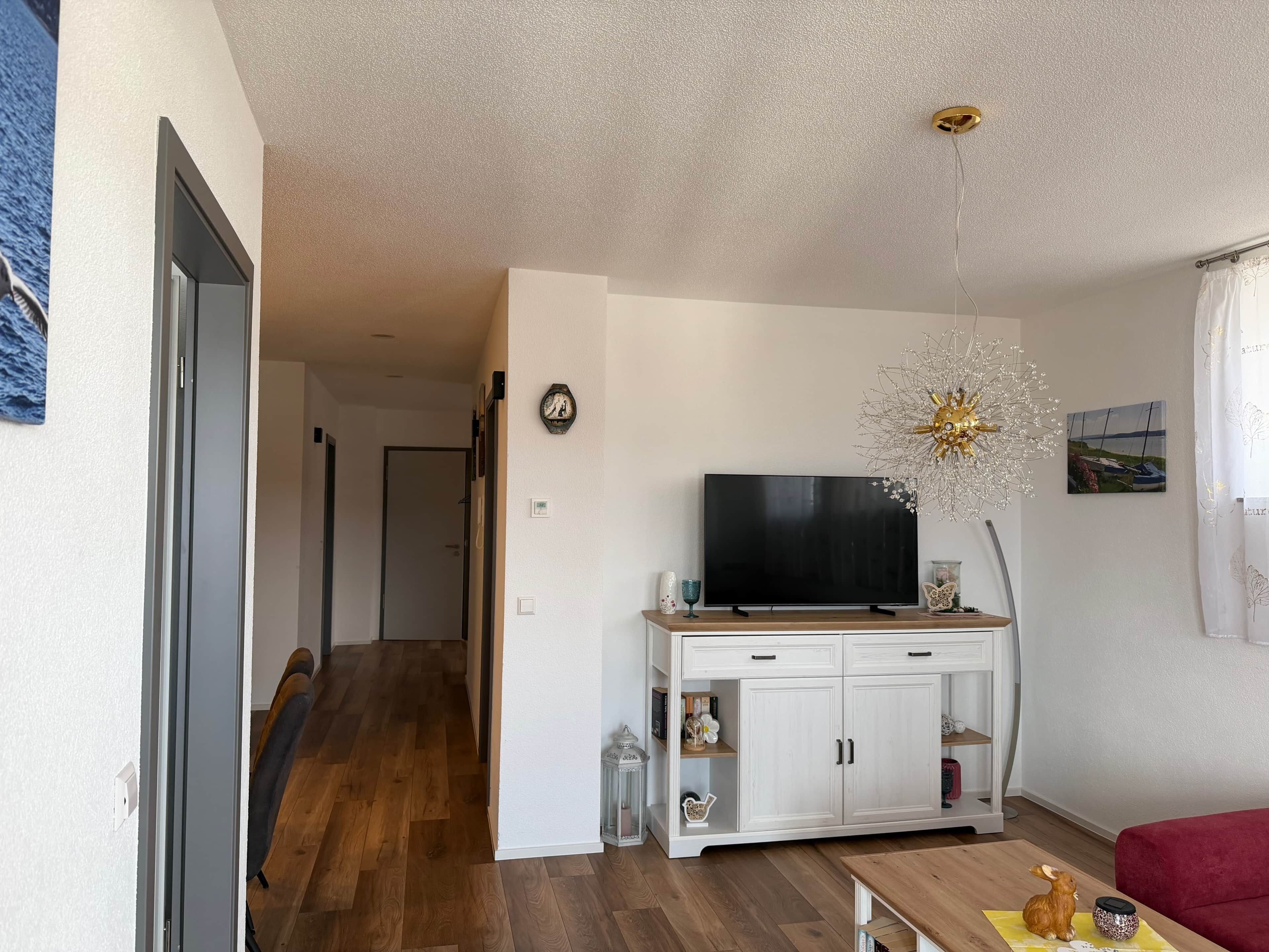 Ein Wohnzimmer mit Fernseher, einer Kommode, einem roten Sofa und Holzboden.