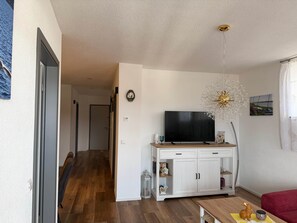 Ein Wohnzimmer mit Fernseher, einer Kommode, einem roten Sofa und Holzboden.