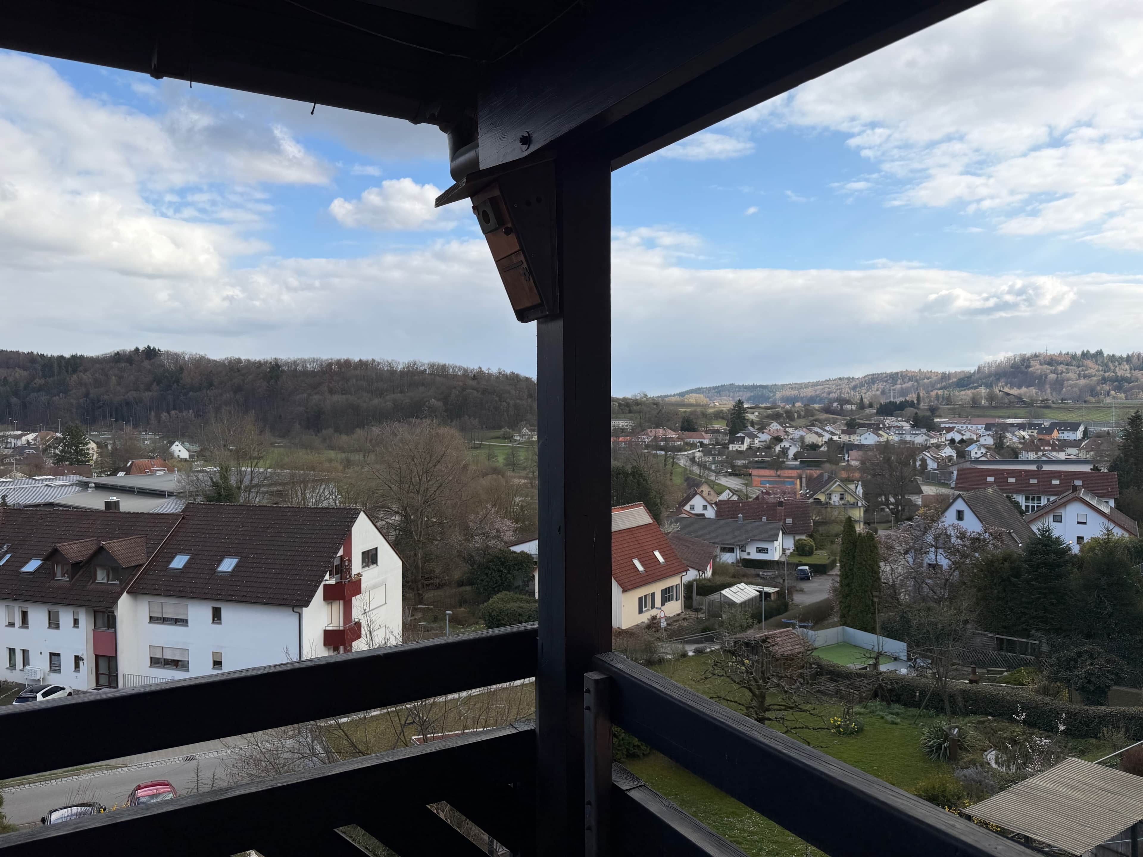 Une vue depuis un balcon donnant sur un quartier résidentiel, avec des maisons et un paysage vallonné en arrière-plan.