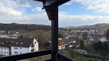 Blick vom Balkon auf ein Wohngebiet mit Häusern und einer hügeligen Landschaft im Hintergrund.