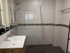 Ein Badezimmer mit einem weißen Waschbecken, einem Spiegel, einer Dusche inklusive Handbrause und einem gefliesten Boden.