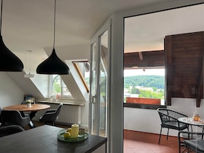 Ein moderner Essbereich mit Tisch, Stühlen und Blick auf eine grüne Landschaft durch große Fenster.