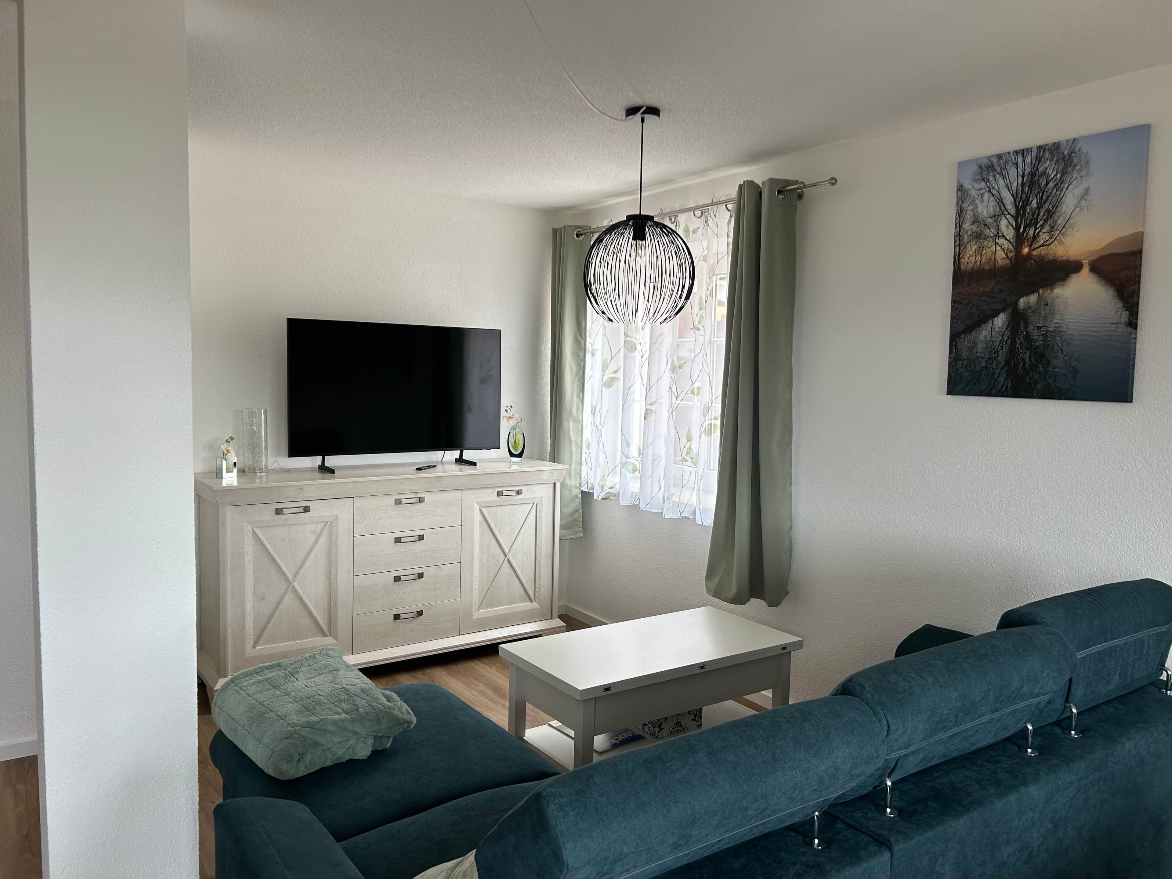Una sala de estar moderna con un televisor de pantalla plana, un mueble blanco, un conjunto de sofá, una mesita y un cuadro en la pared.