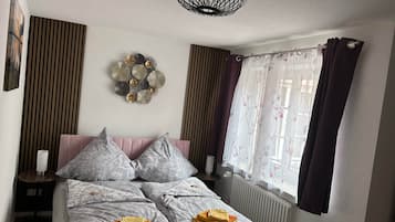 A neatly made bed with pillows and folded towels, a wall-mounted decorative item, a bedside table with a lamp, and a window with curtains.