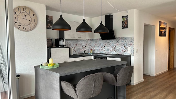 Una cocina moderna con una isla central, luces colgantes y un reloj en la pared.