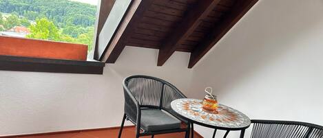 A balcony with a table and two chairs, a view of greenery, and a wooden ceiling.