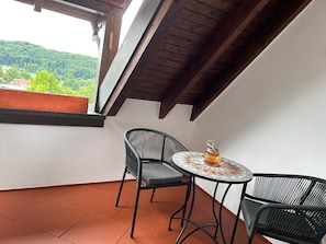 Ein Balkon mit Tisch und zwei Stühlen, Blick ins Grüne und Holzboden.