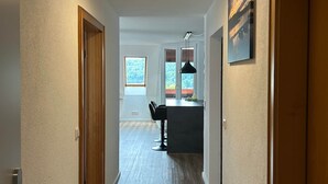Un pasillo con piso de madera, una zona de cocina con barra y taburetes, y una mesa de comedor.