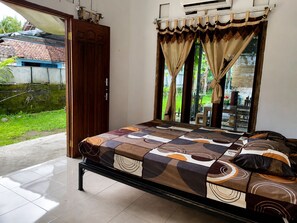 Ein Schlafzimmer mit Bett, Vorhängen, einer Schiebetür aus Glas und Blick ins Freie.