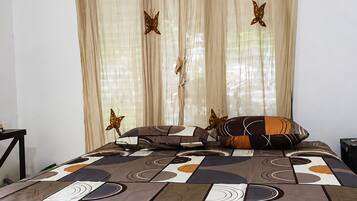 A hotel room with a bed, a nightstand, an air conditioning unit, and curtains with butterfly designs.