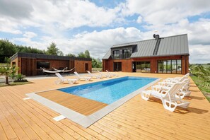 A modern outdoor swimming pool area with lounge chairs and a wooden deck.