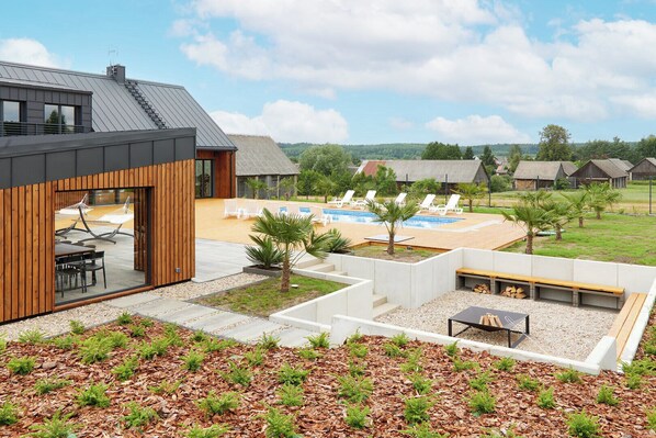 Un espacio exterior moderno con piscina, sillones de descanso y una terraza de madera.