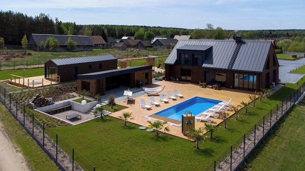 A modern house with a large swimming pool, outdoor seating, and a well-maintained lawn.