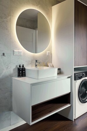 Un baño moderno con un espejo redondo, tocador blanco y lavadora integrada.