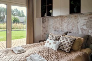 A bedroom with a large bed, a view of the outdoors, and a wooden headboard.