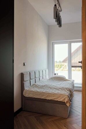 Een moderne slaapkamer met een groot bed, een plafondlamp en uitzicht door een glazen deur.
