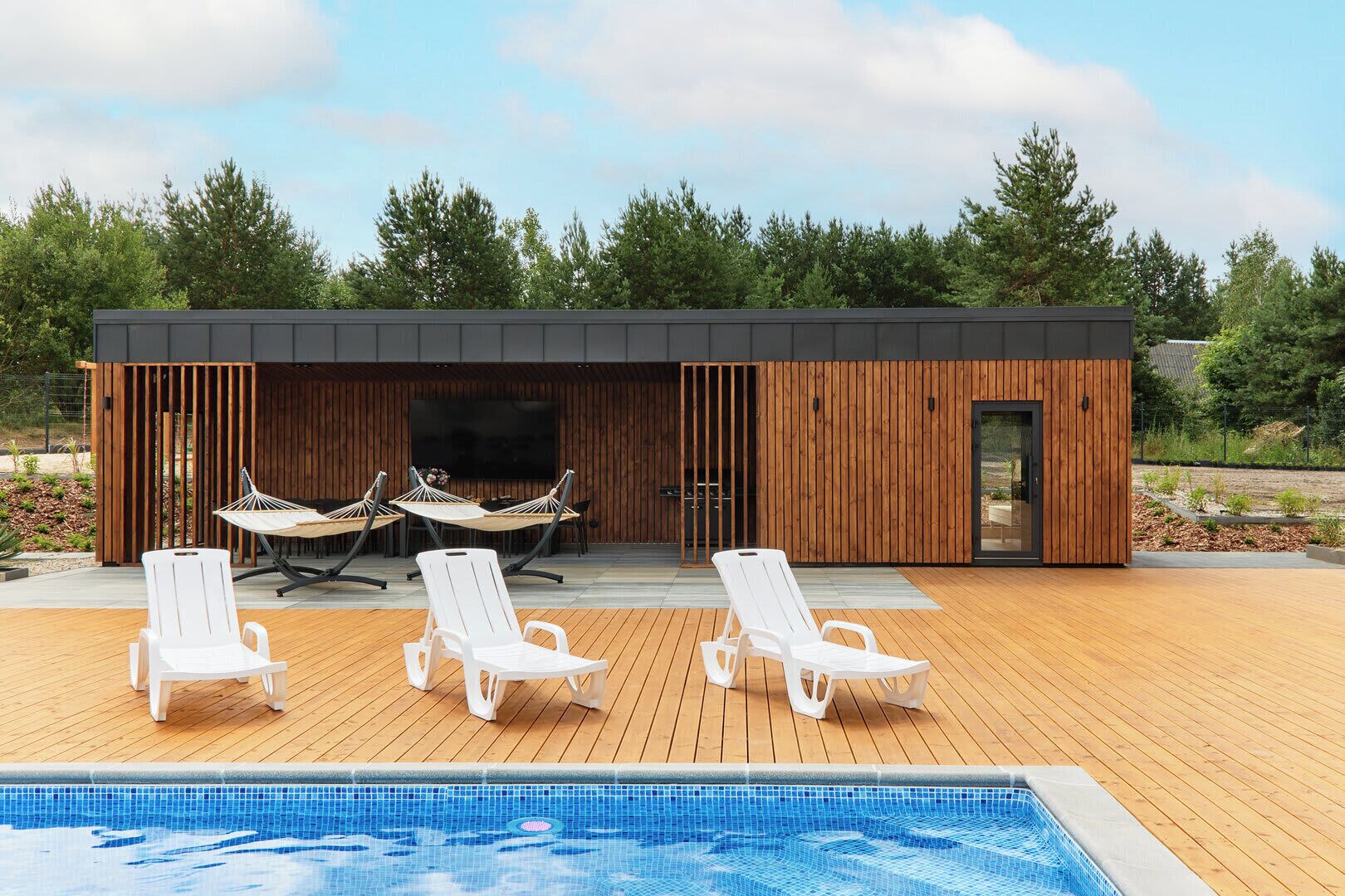 Een modern zwembadgedeelte buiten, met ligbedden en een houten terras.