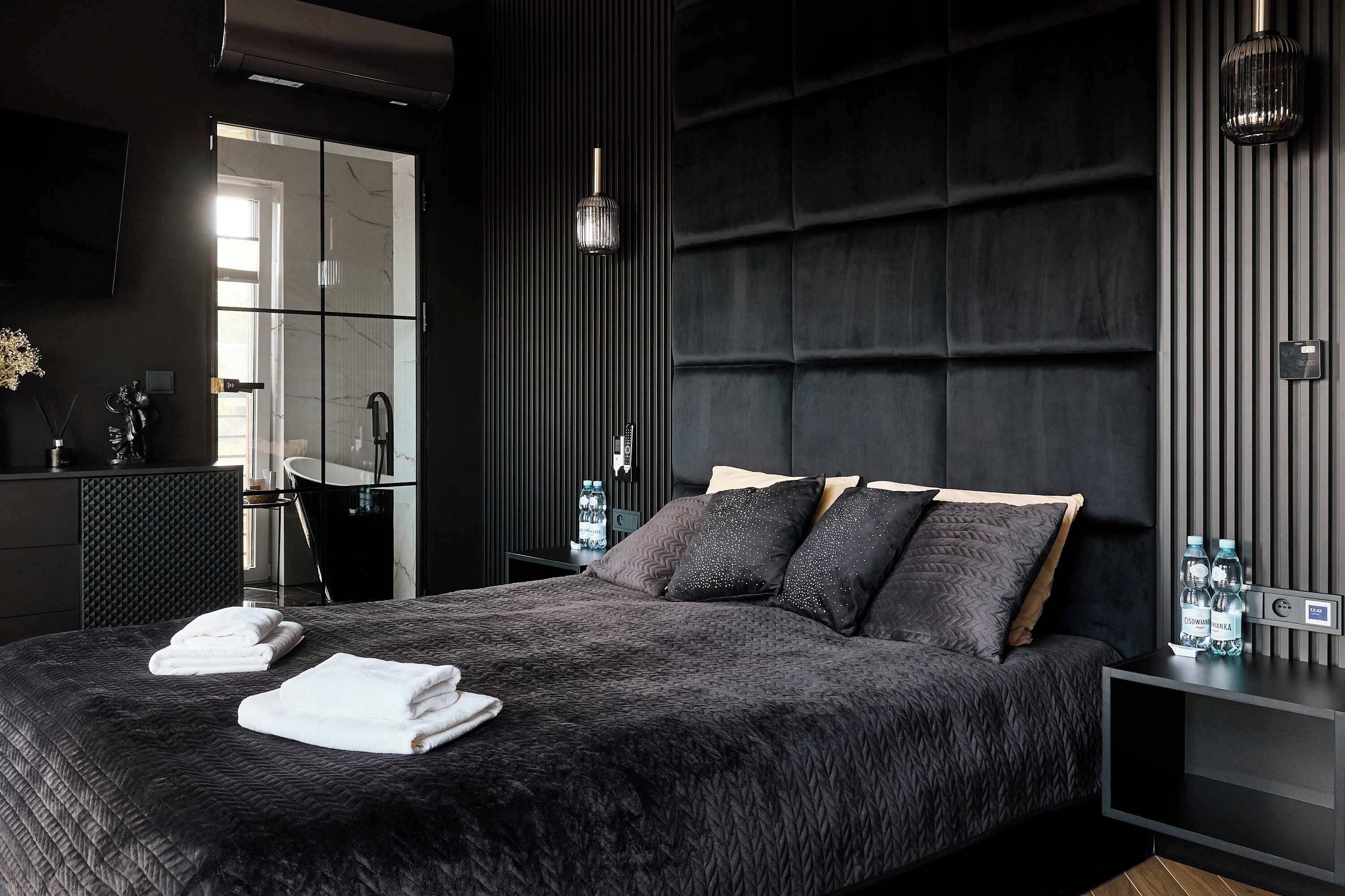 Een moderne slaapkamer met een groot bed, een nachtkastje, een spiegel en een bijzettafeltje.