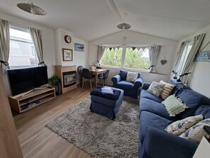 A cozy living room with a television, sofa, ottoman, and fireplace. - Demelza Seven Bays Holiday Park (Padstow)