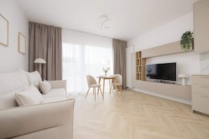 Ein modernes Wohnzimmer mit einer Couch, einem Esstisch mit Stühlen, einem Fernseher und einer Pflanze.
